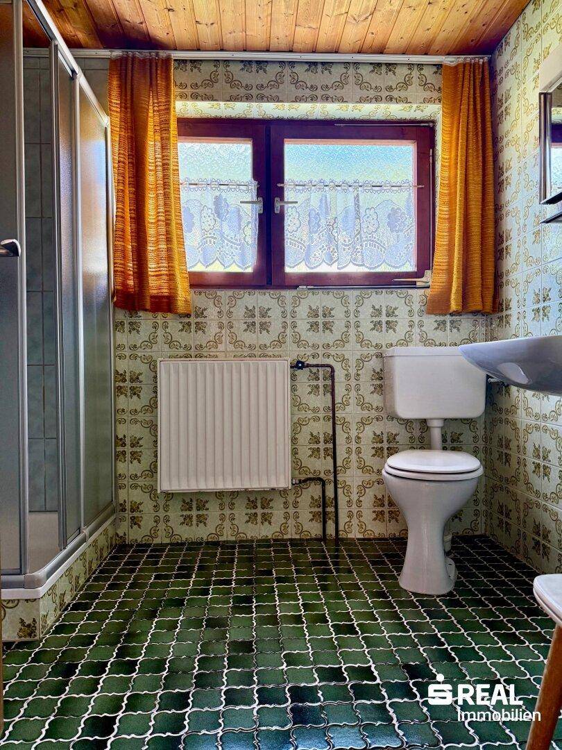 Badezimmer mit Duschkabine, WC und auffälligen grünen Bodenfliesen im Vintage-Stil.