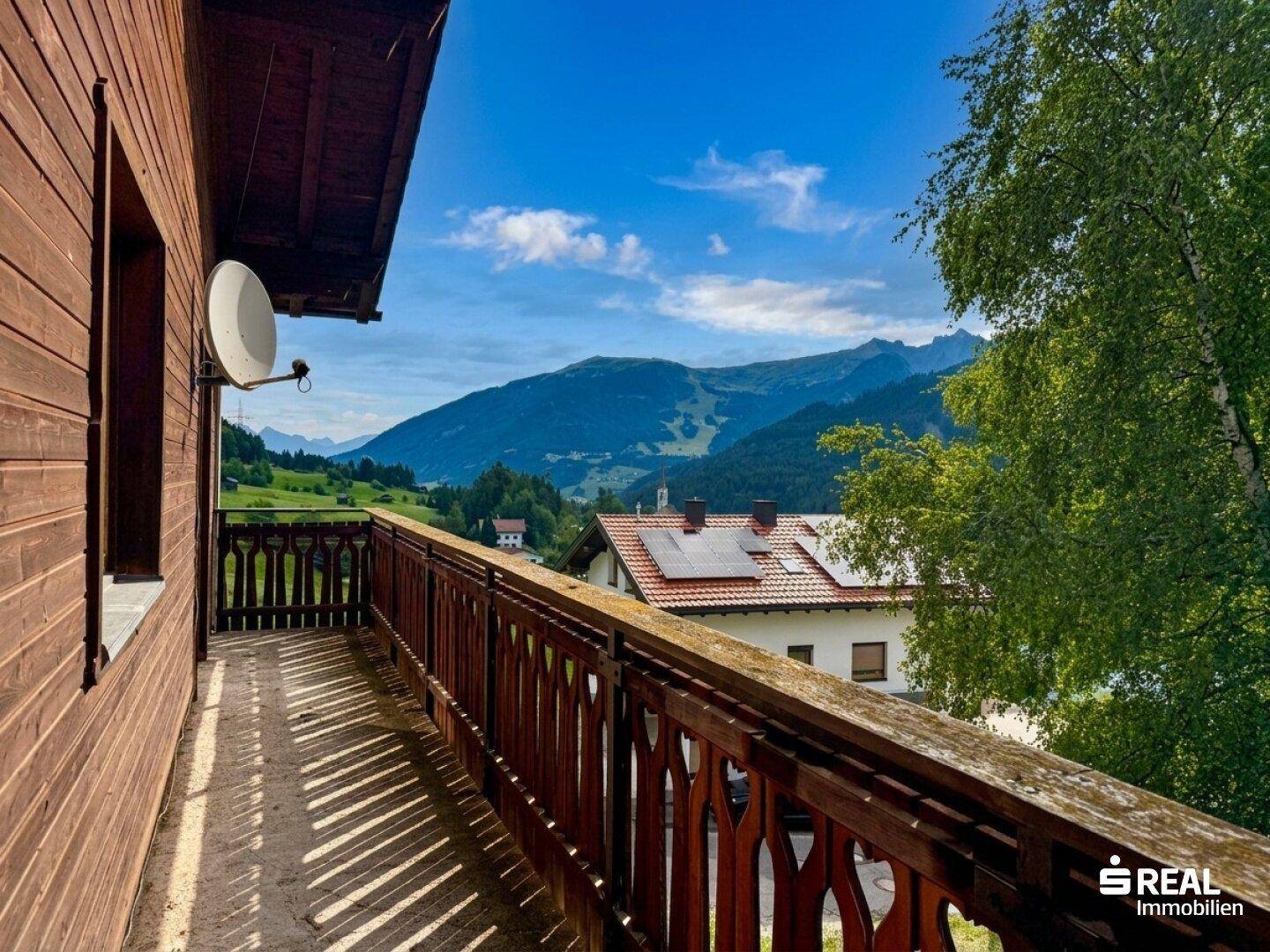 Holzbalkon mit geschnitztem Geländer und weitem Blick auf die umliegende Berglandschaft.