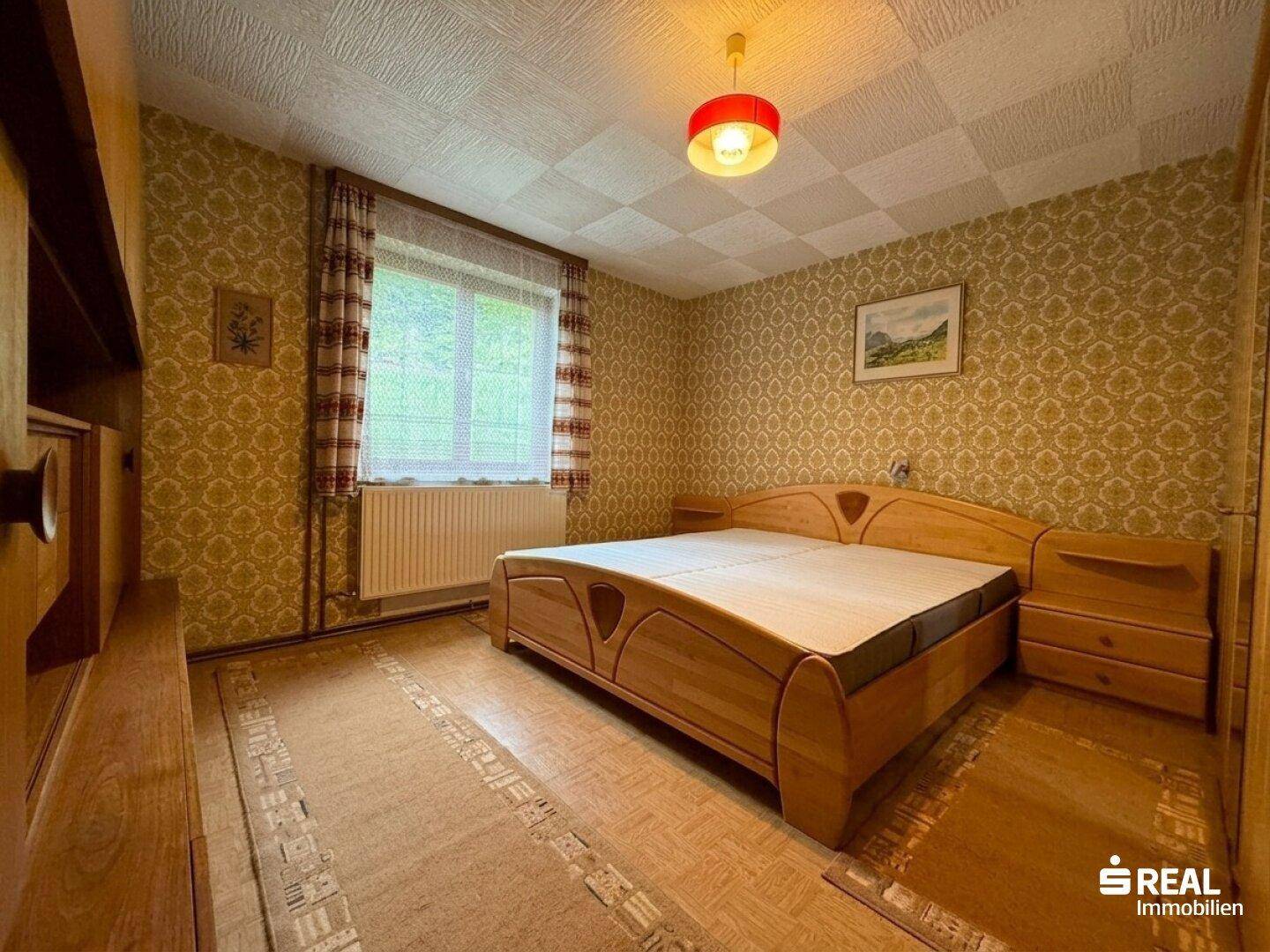 Schlafzimmer mit Doppelbett, gemusterter Tapete und Teppichboden in warmen Farbtönen.