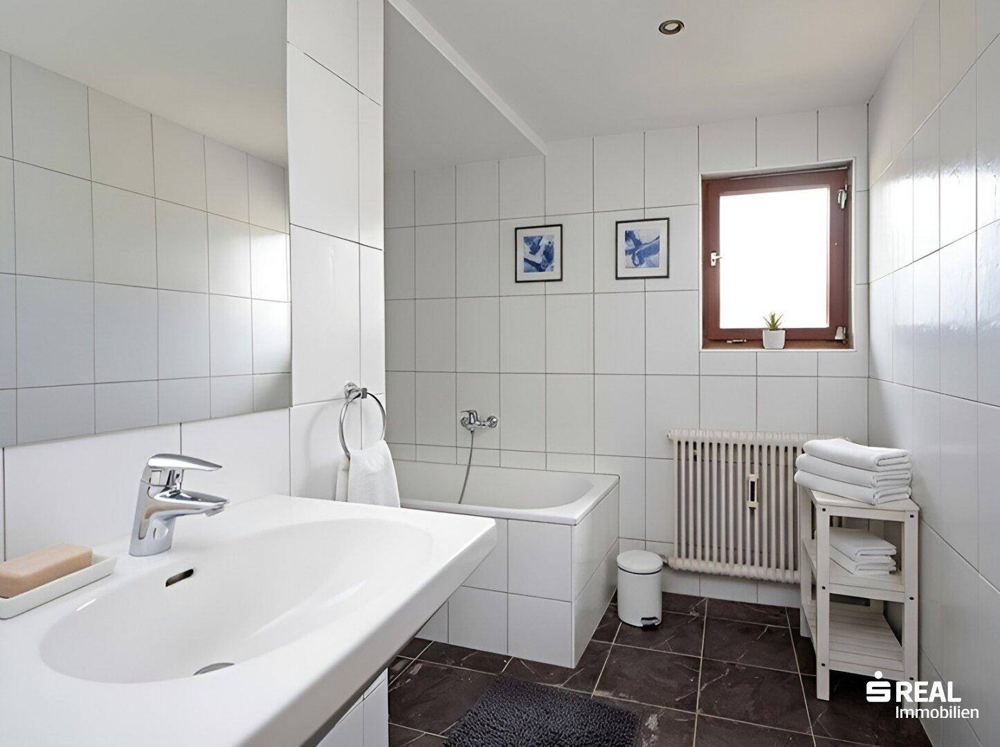 Helles Badezimmer mit Badewanne, Fenster, weißen Fliesen und modernem Waschtisch.