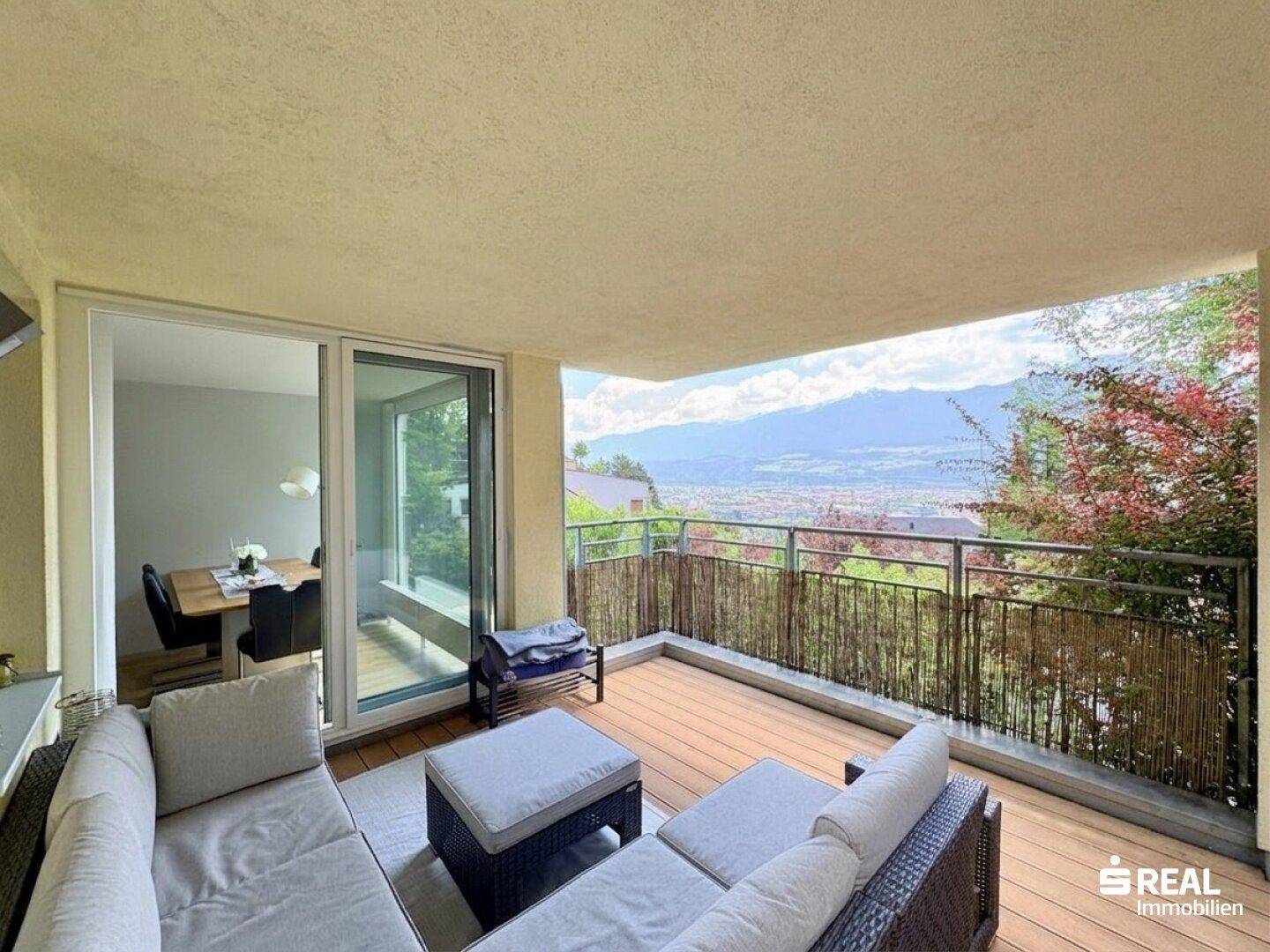 Großer überdachter Balkon mit bequemen Loungemöbeln und Panoramablick auf die Stadt und Berge.