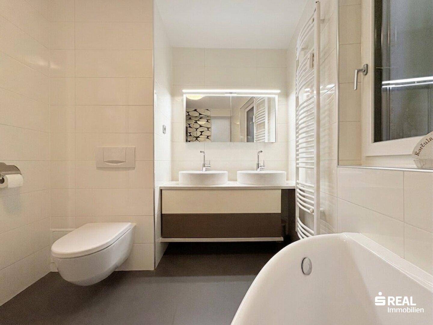 Elegantes Badezimmer mit Doppelwaschbecken, Wand-WC und großer Badewanne.
