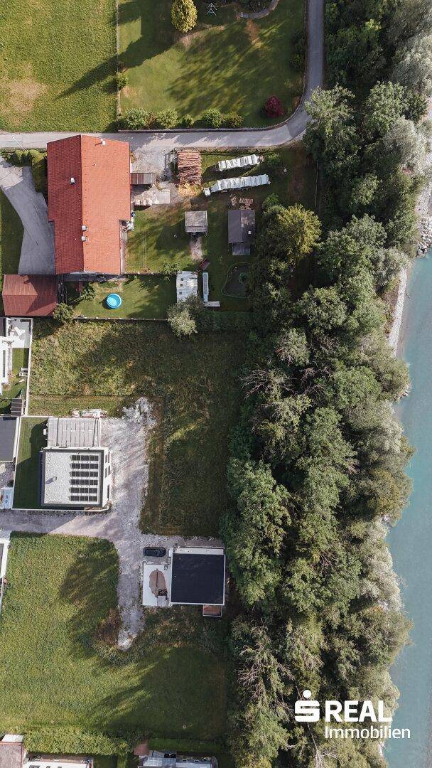 Vertikale Luftaufnahme einer Wohnsiedlung am Flussufer mit viel Grün und einzelnen Häusern.