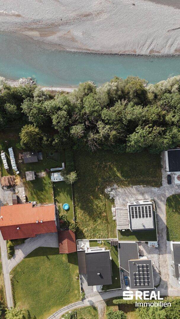 Vertikale Luftaufnahme einer Wohnsiedlung am Flussufer mit viel Grün und einzelnen Häusern.