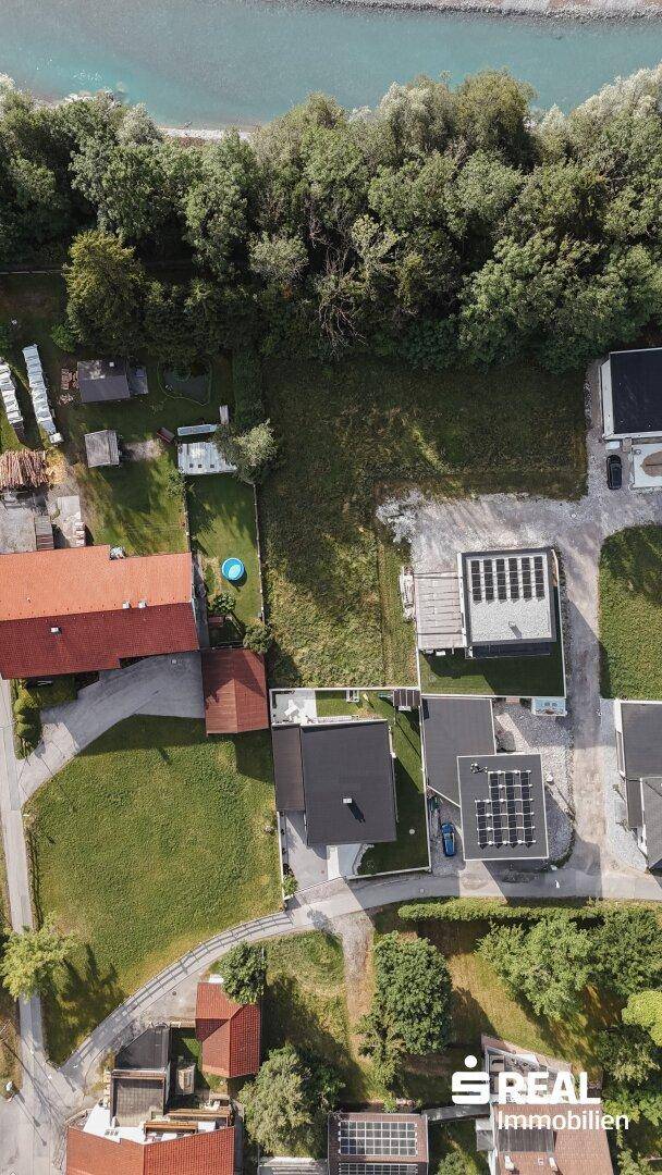 Vertikale Luftaufnahme einer Wohnsiedlung am Flussufer mit viel Grün und einzelnen Häusern.