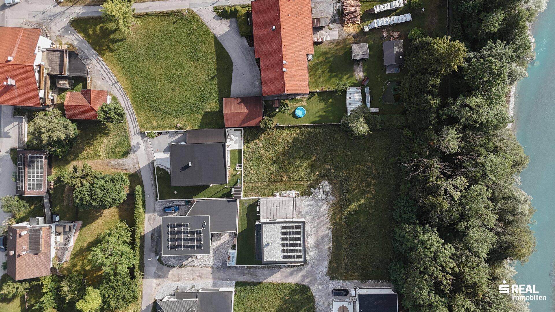 Vertikale Luftaufnahme einer Wohnsiedlung am Flussufer mit viel Grün und einzelnen Häusern.