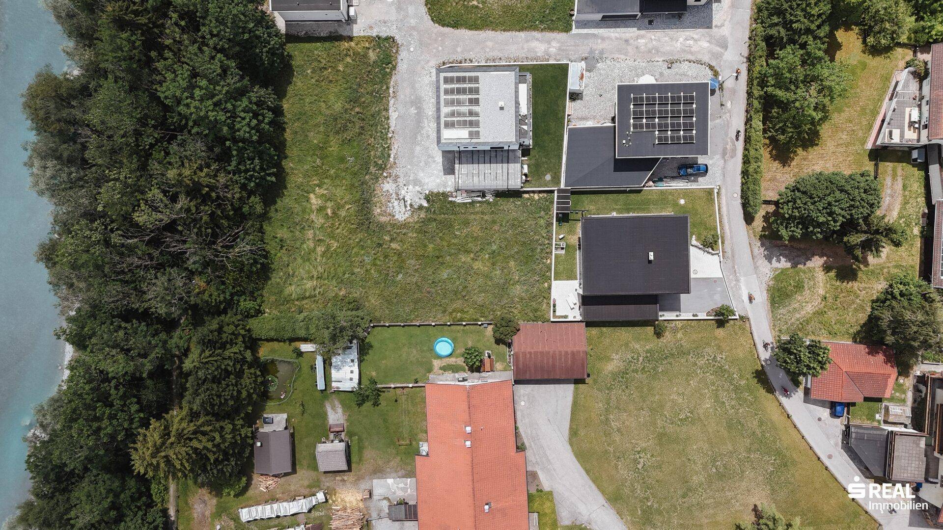 Vertikale Luftaufnahme einer Wohnsiedlung am Flussufer mit viel Grün und einzelnen Häusern.