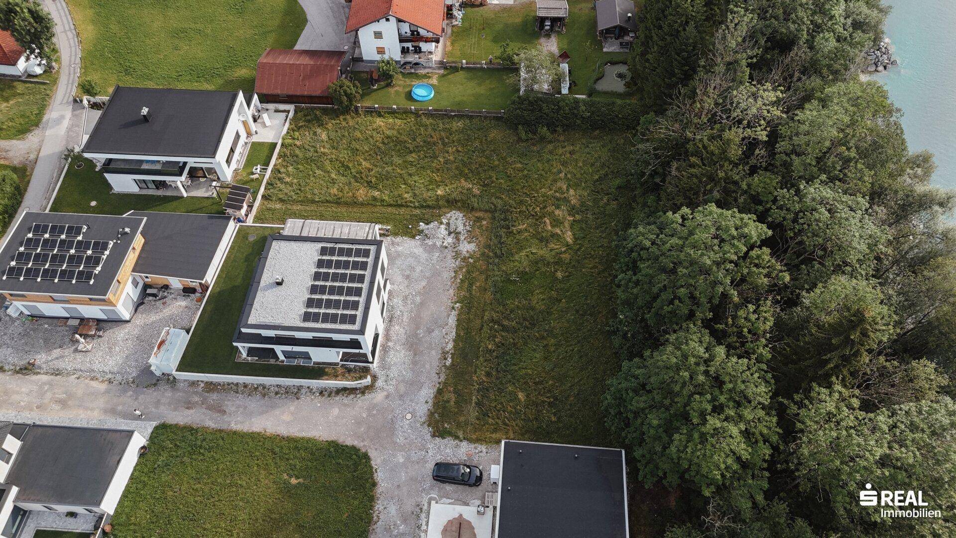 Weitläufige Luftaufnahme eines Baugrundstücks mit angrenzendem Fluss und modernen Häusern.