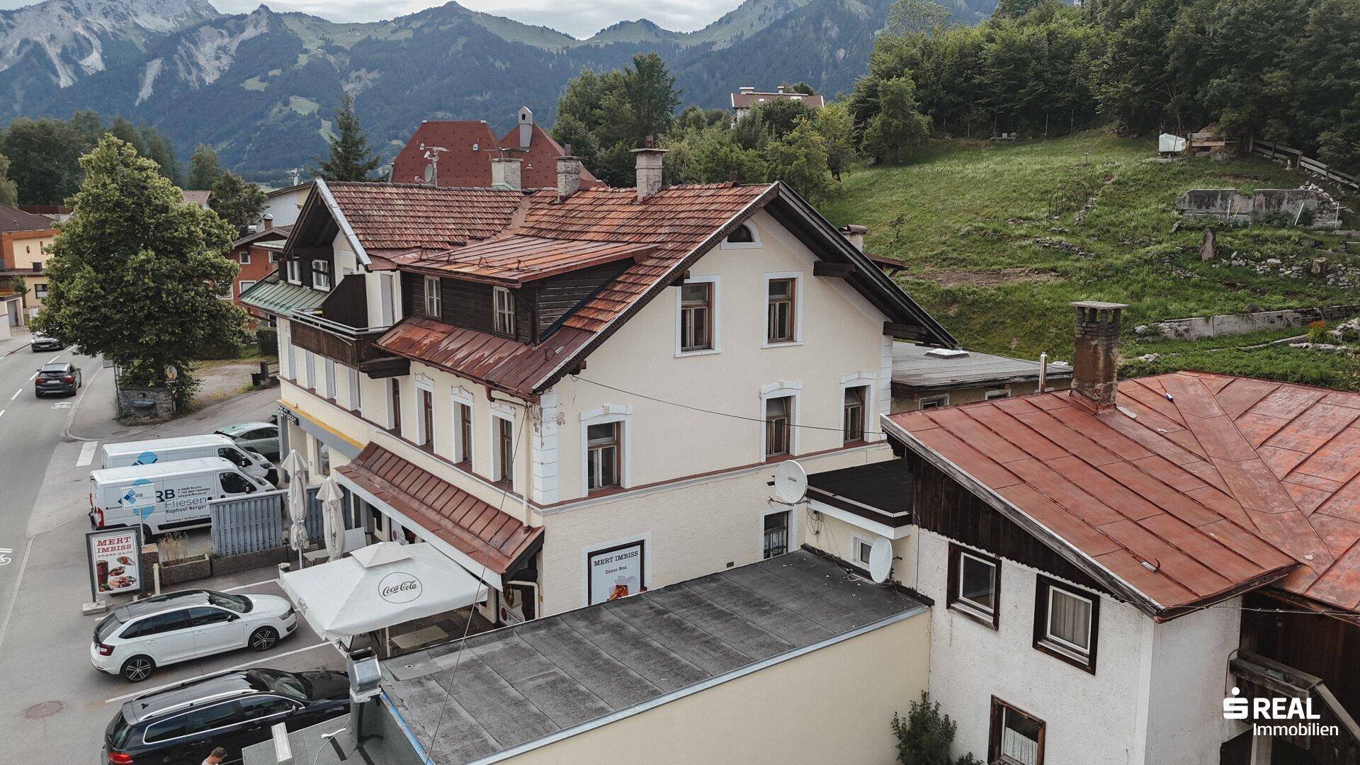 Panoramablick auf das Gebäudeensemble mit traditioneller Architektur vor einer Bergkulisse.