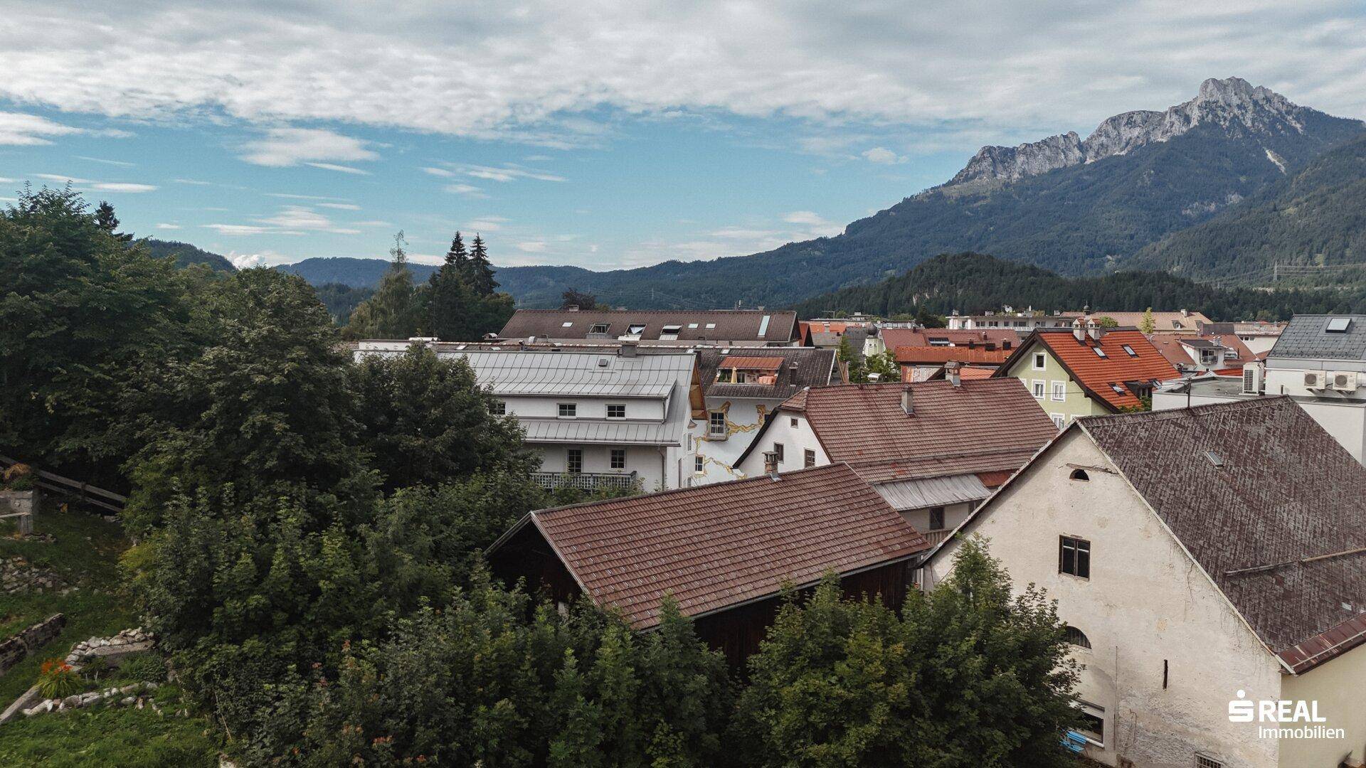 Weitläufiger Blick über eine Wohnsiedlung mit vielen Dächern und einer beeindruckenden Berglandschaft.