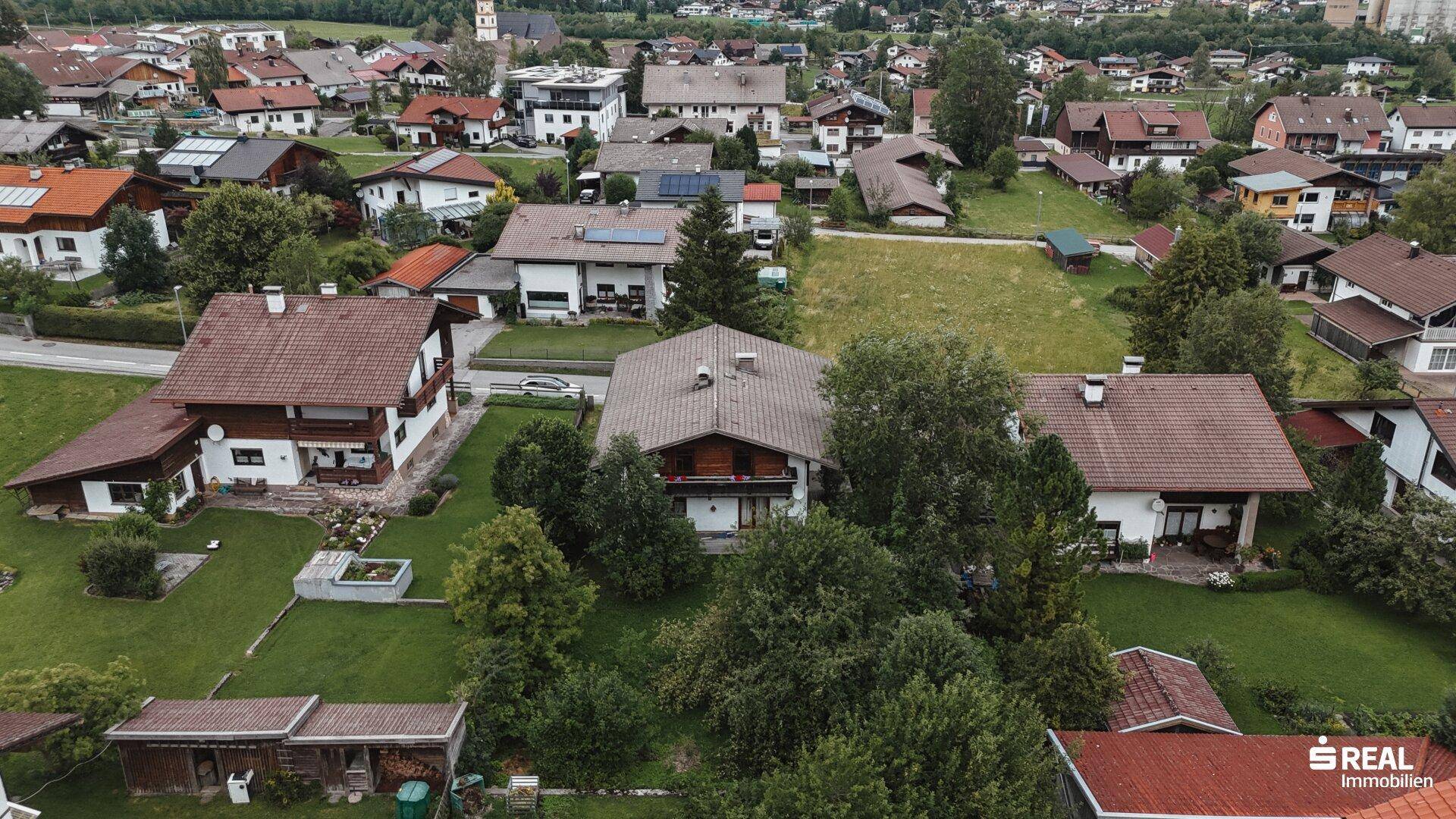 Luftaufnahme des Hauses mit umliegenden Gärten und der weiteren Wohnsiedlung im Hintergrund.