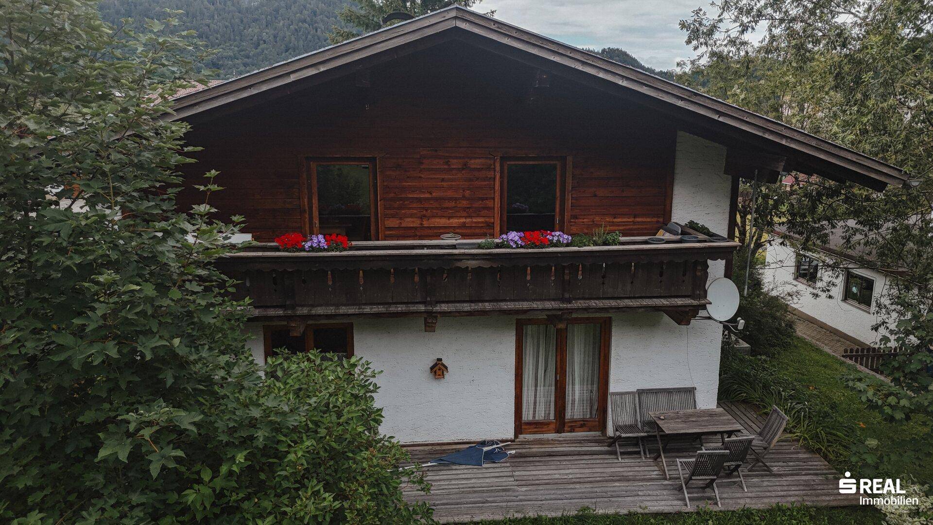 Traditionelles Haus mit Holzbalkon und einer möblierten Holzterrasse im Erdgeschoss.