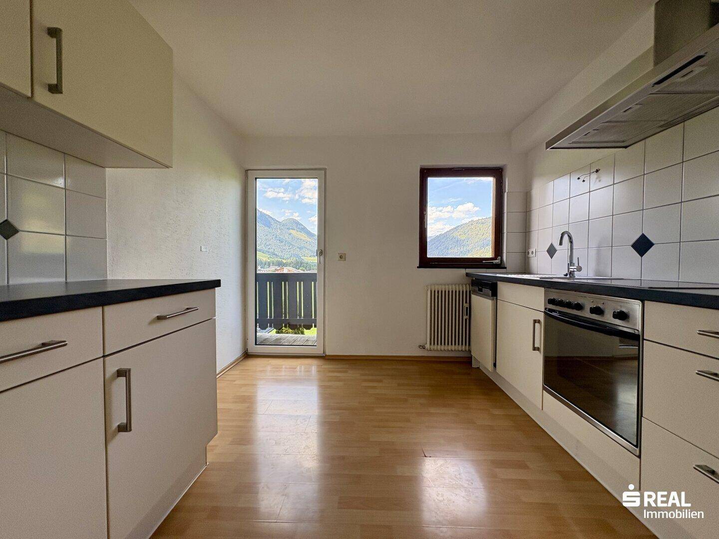 Leere Küche mit Einbauschränken, Fliesenboden und herrlichem Bergblick durch das Fenster.