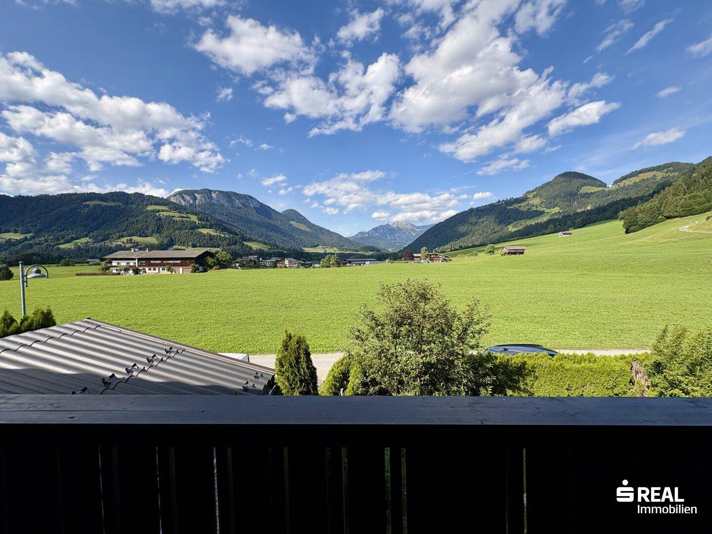 Weitläufiger Panoramablick von einem Balkon über grüne Felder und majestätische Berge.