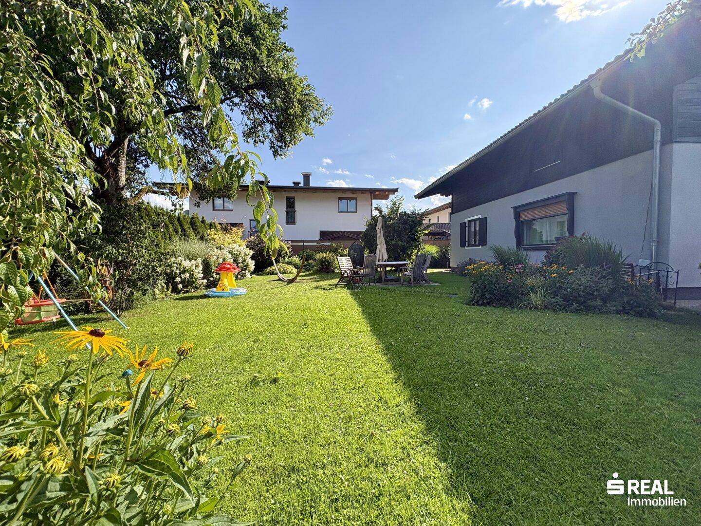 Großer, gepflegter Garten mit Rasenfläche, altem Baumbestand und Spielgeräten.