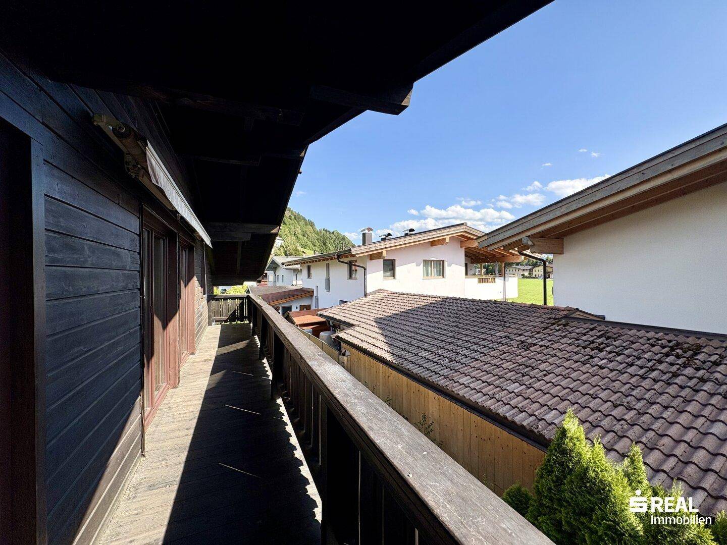 Langer Holzbalkon mit Blick auf die Dächer der Nachbarhäuser und die umliegende Landschaft.