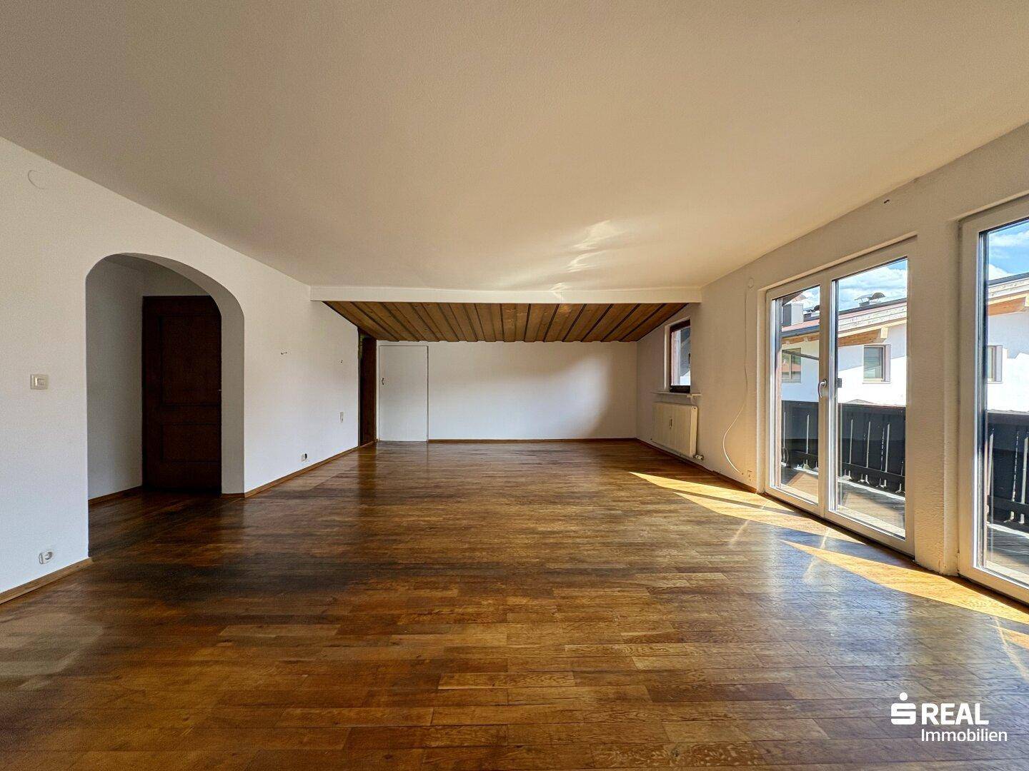 Helles Wohnzimmer mit Holzbalkendecke, Parkettboden und großen Fenstern für viel Tageslicht.