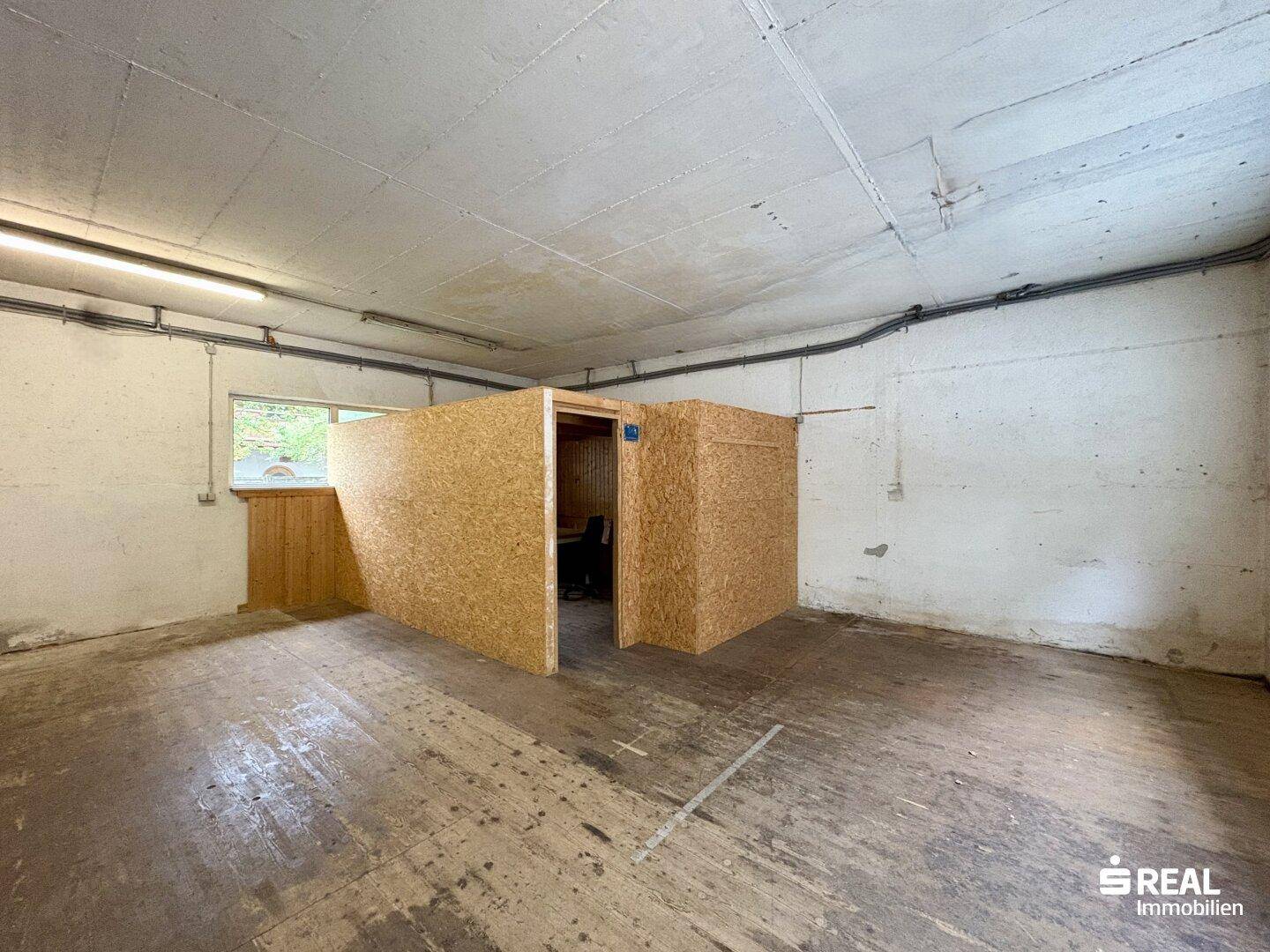 Großer Lagerraum mit Betonboden und einer eingebauten Holzkabine, vielseitig nutzbar.