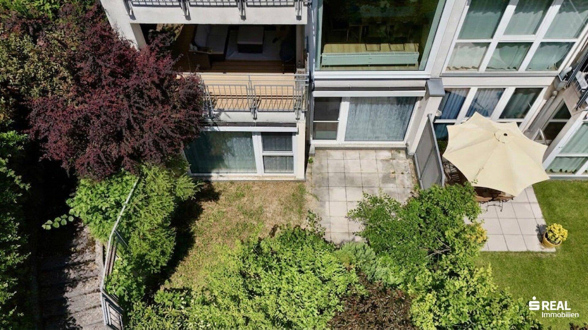 Gepflegter Gartenbereich mit Terrasse, Sonnenschirm und üppiger Bepflanzung.