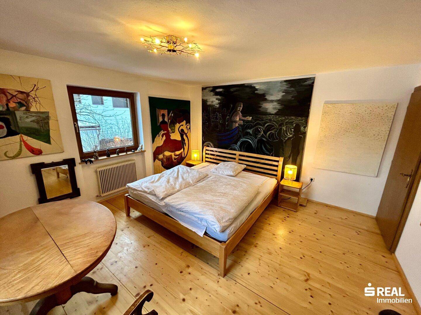 Schlafzimmer mit Doppelbett, Holzboden und großen Fenstern für viel Tageslicht.