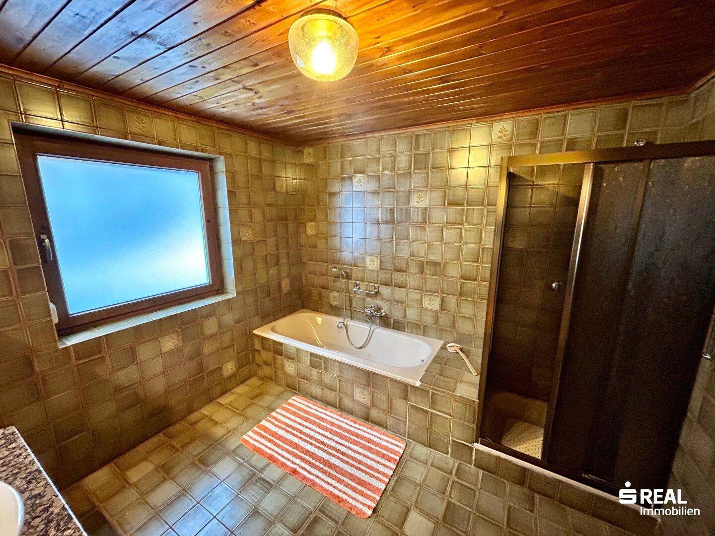 Badezimmer mit Badewanne, Duschkabine, Fliesenboden und Holzdecke.