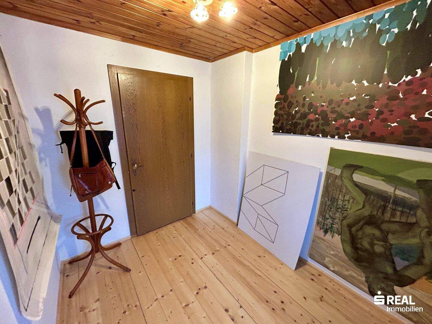 Flur mit Holzboden, Garderobe und Kunstwerken an den Wänden.