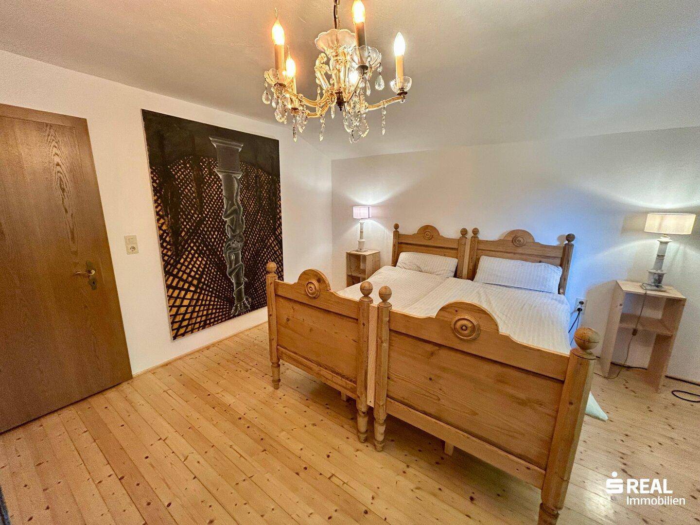 Schlafzimmer mit zwei Einzelbetten, Holzboden und einem eleganten Kronleuchter.