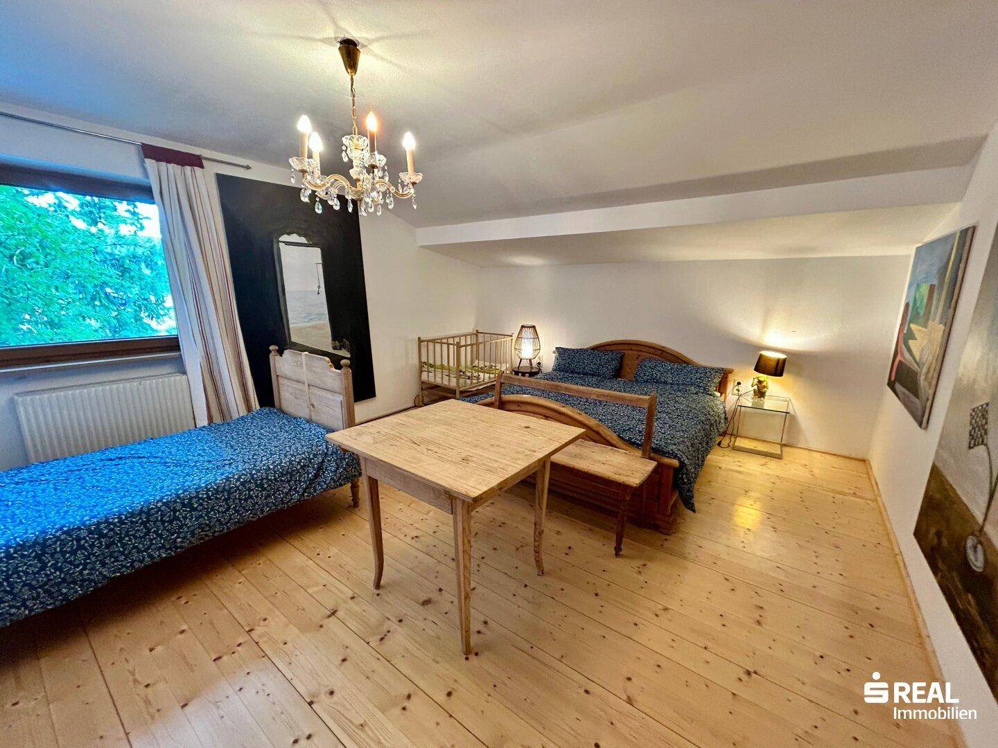Geräumiges Schlafzimmer mit Holzboden, großem Bett und einem kleinen Tisch am Fenster.