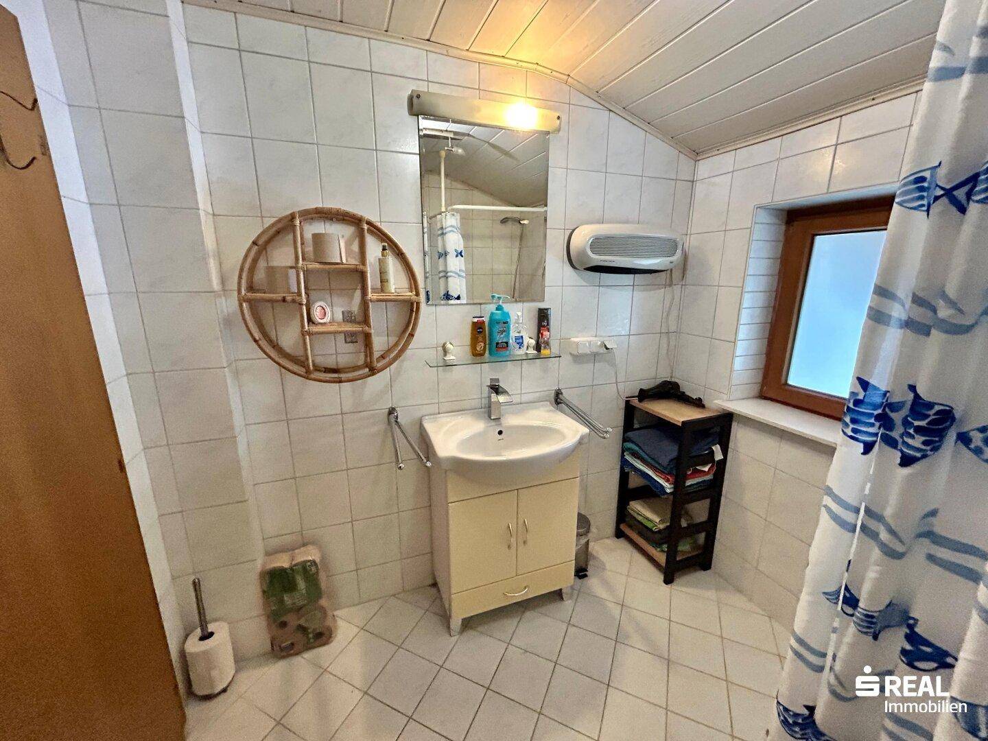 Helles Badezimmer mit Waschbecken, Spiegel und weiß gefliesten Wänden.
