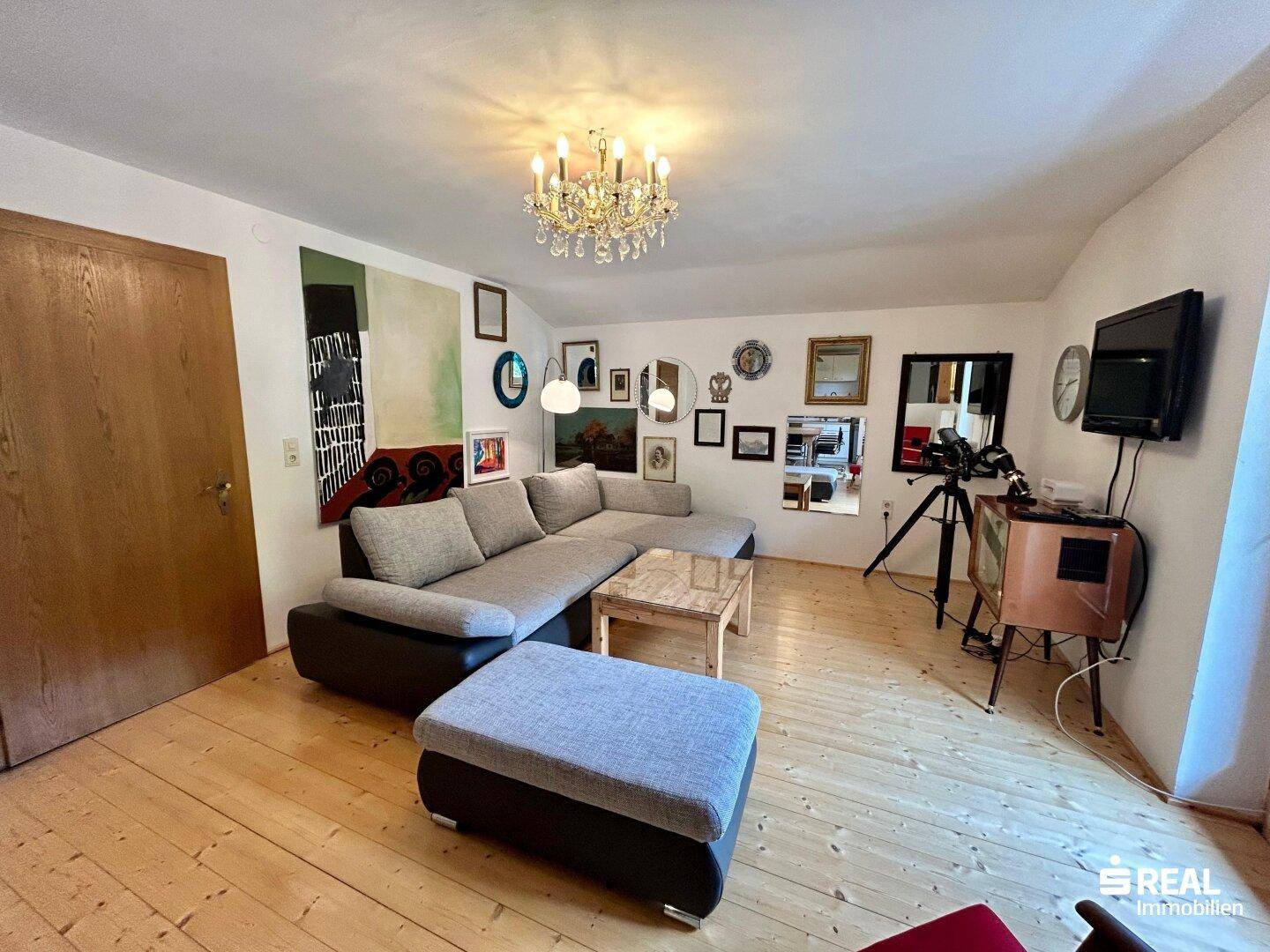 Helles Wohnzimmer mit großem Ecksofa, Holzboden und einem Kronleuchter an der Decke.