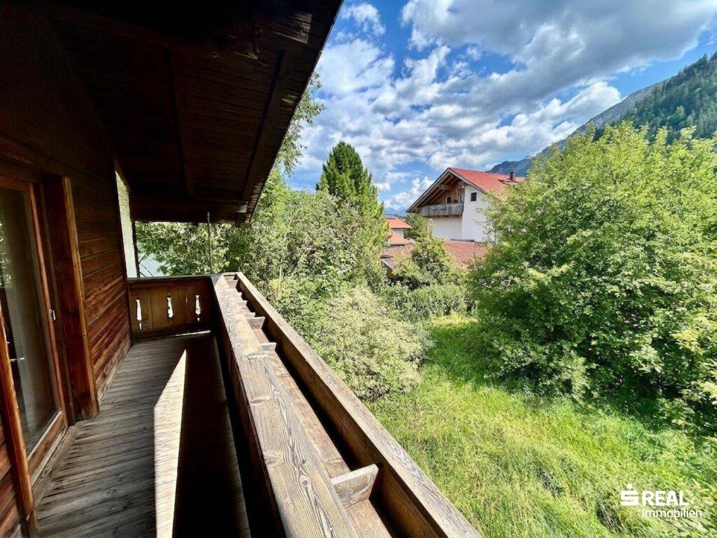 Holzbalkon mit Blick auf die grüne Umgebung und die umliegenden Häuser.