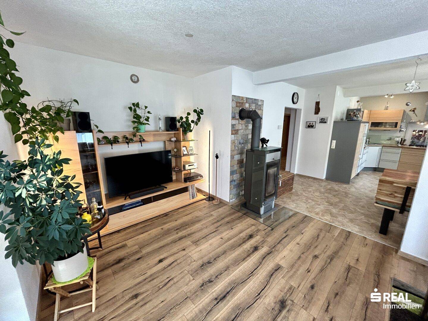 Gemütliches Wohnzimmer mit Holzboden, Kaminofen und offenem Übergang zur Küche.