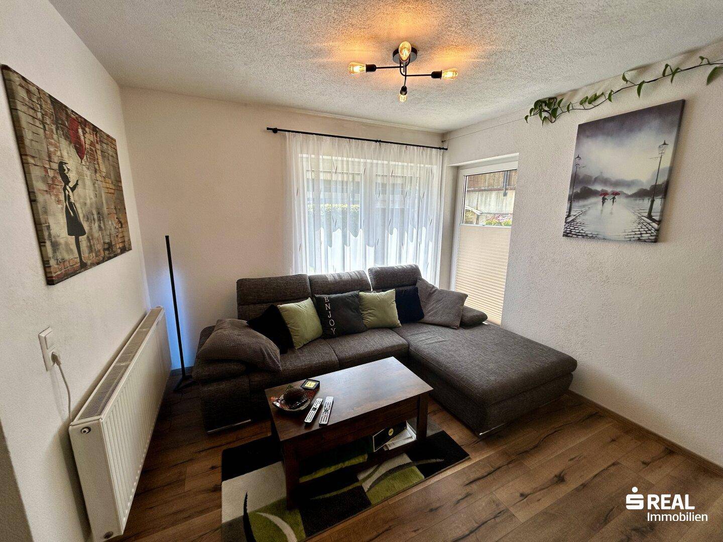 Heller Wohnbereich mit Ecksofa, Couchtisch und Fenster mit Blick nach draußen.