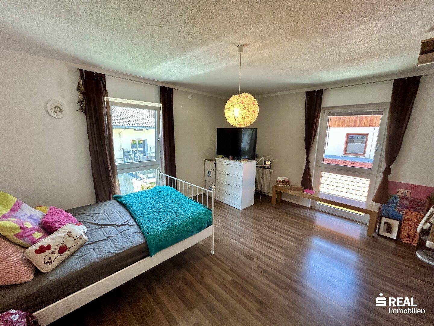 Schlafzimmer mit Einzelbett, Holzboden und zwei Fenstern für eine helle Atmosphäre.
