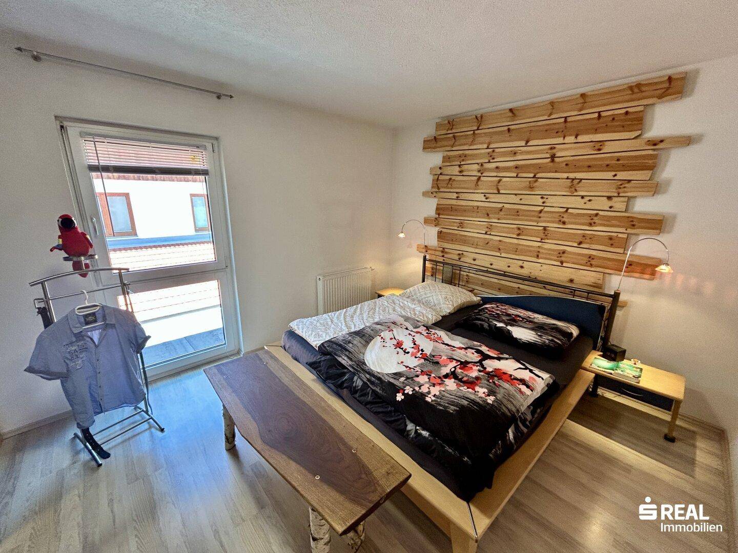 Gemütliches Schlafzimmer mit Doppelbett, Holzkopfteil und Fenster mit Ausblick.