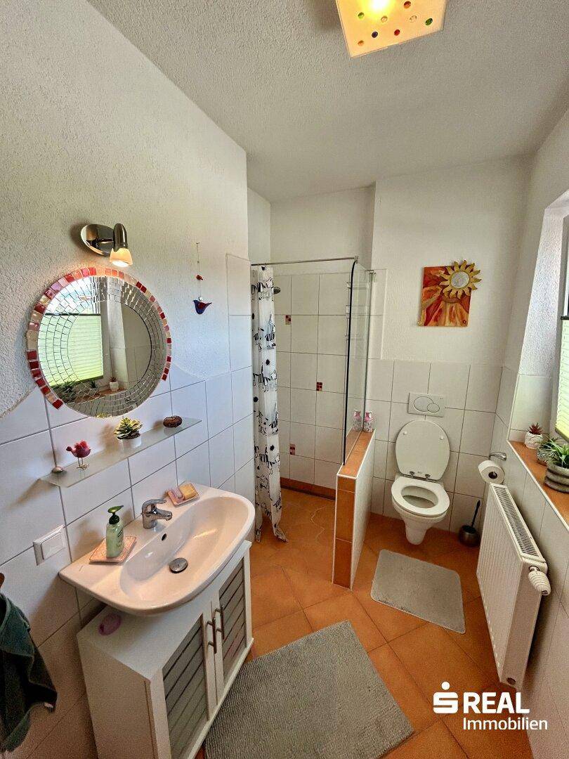 Badezimmer mit Dusche, WC, Waschbecken und Fenster, gefliest in warmen Farbtönen.