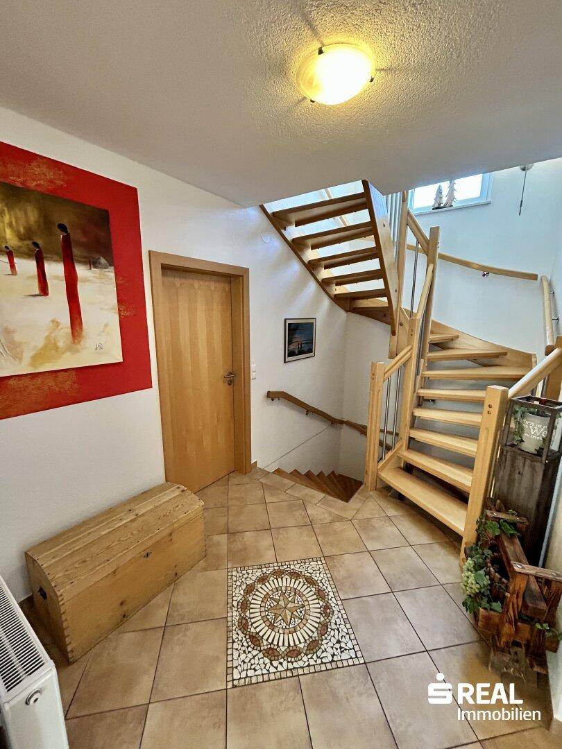 Heller Flur mit Holztreppe, Fliesenboden und dekorativer Wandkunst.