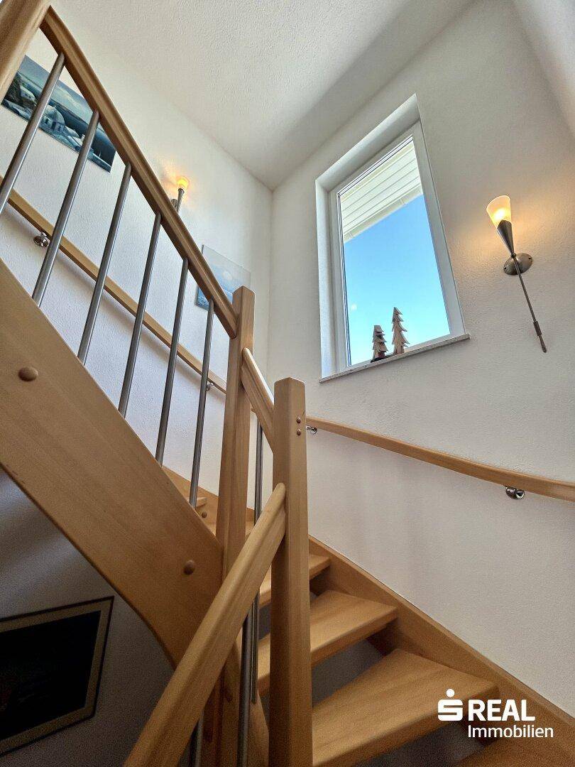 Detailansicht der Holztreppe mit Geländer und Fenster, das Tageslicht hereinlässt.