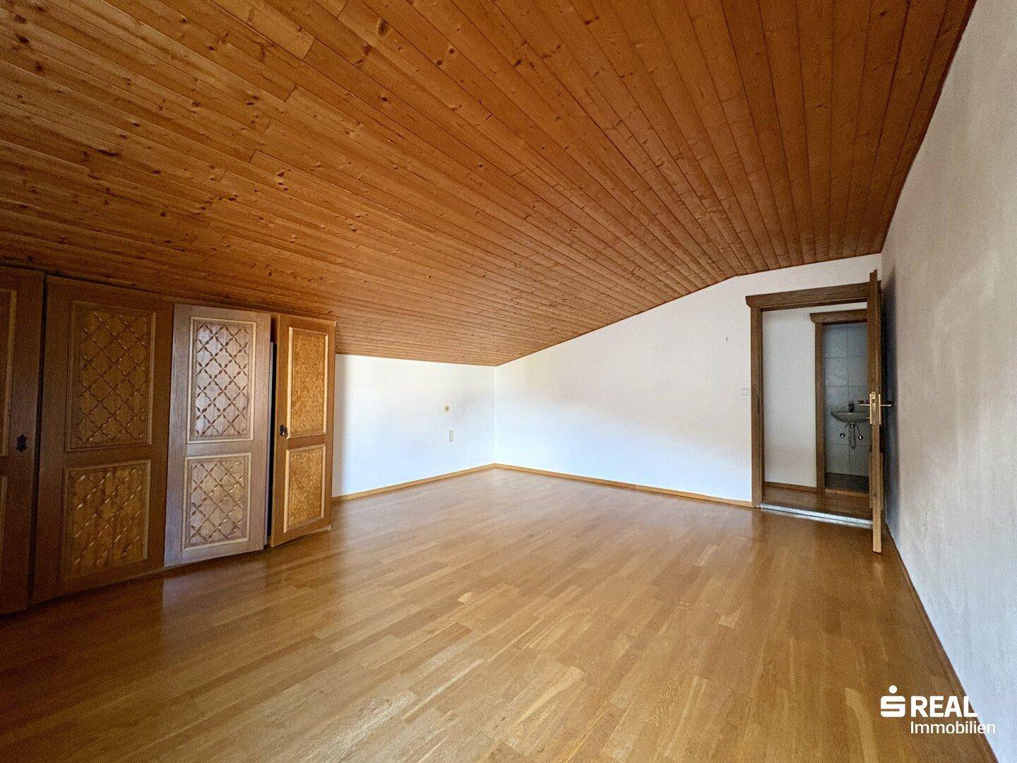 Helles Schlafzimmer im Dachgeschoss mit Holzdeckenverkleidung, Einbauschränken und Holzboden.