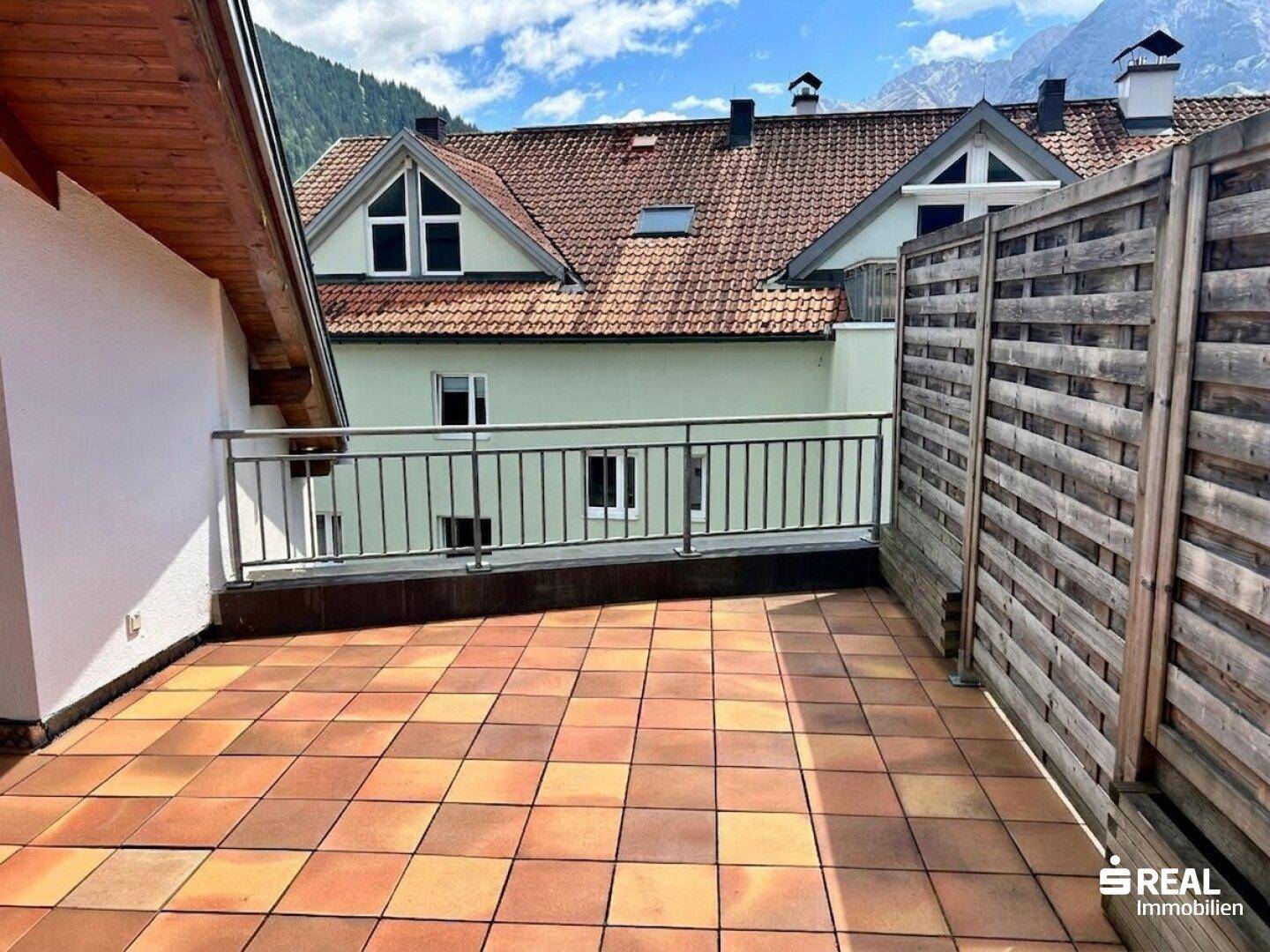 Große Terrasse mit Metallgeländer und Blick auf umliegende Gebäude und Berge.