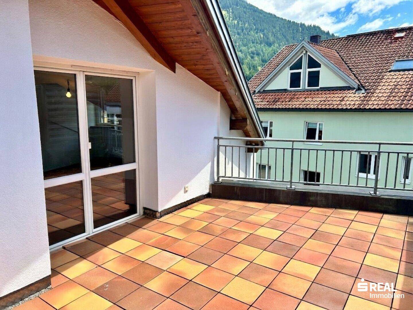 Sonnige Terrasse mit Bergblick und Zugang zu den Innenräumen durch große Fenster.