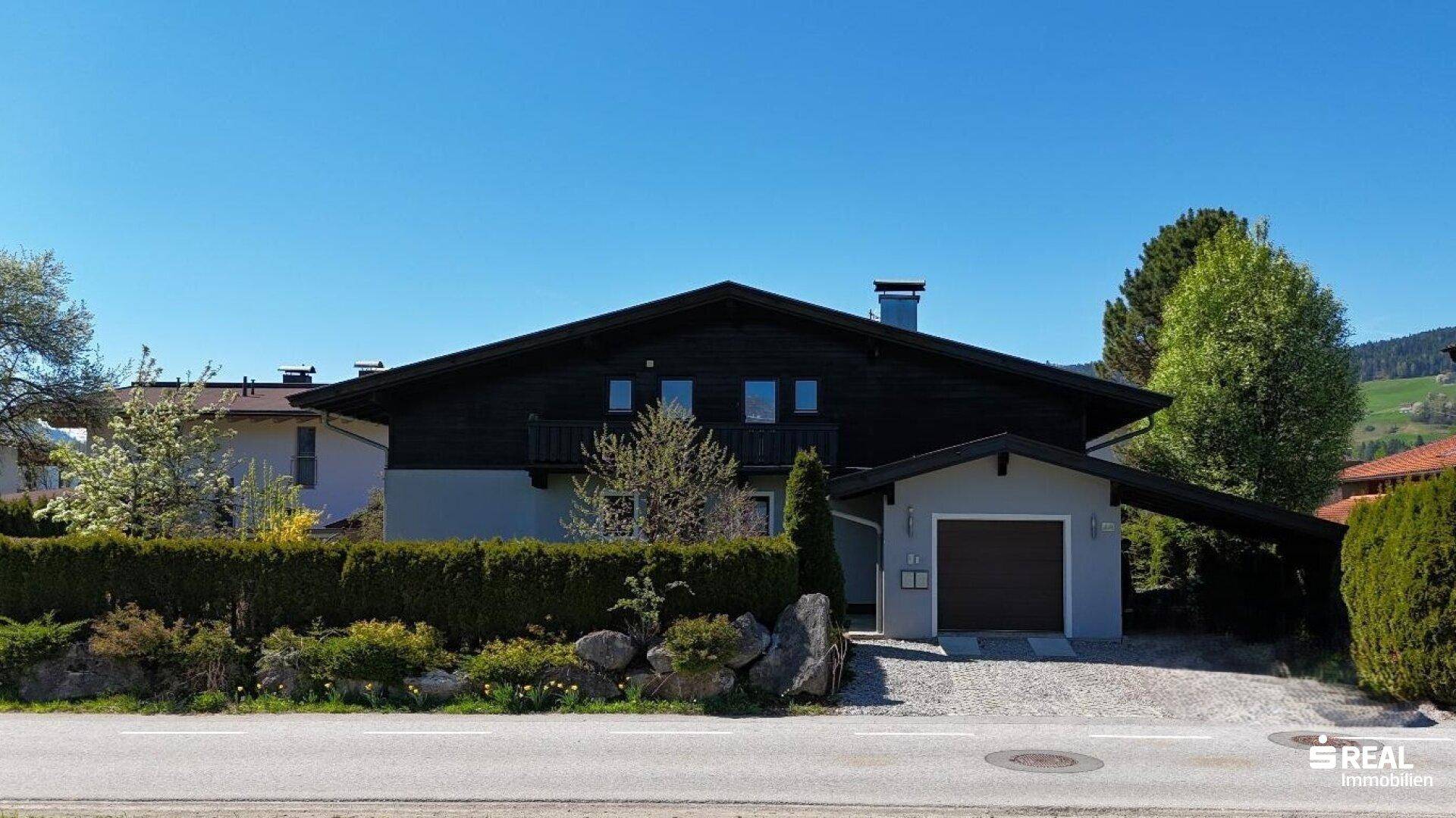 Traditionelles Haus im Chalet-Stil mit Holzfassade, Satteldach, Garage und gepflegtem Vorgarten.