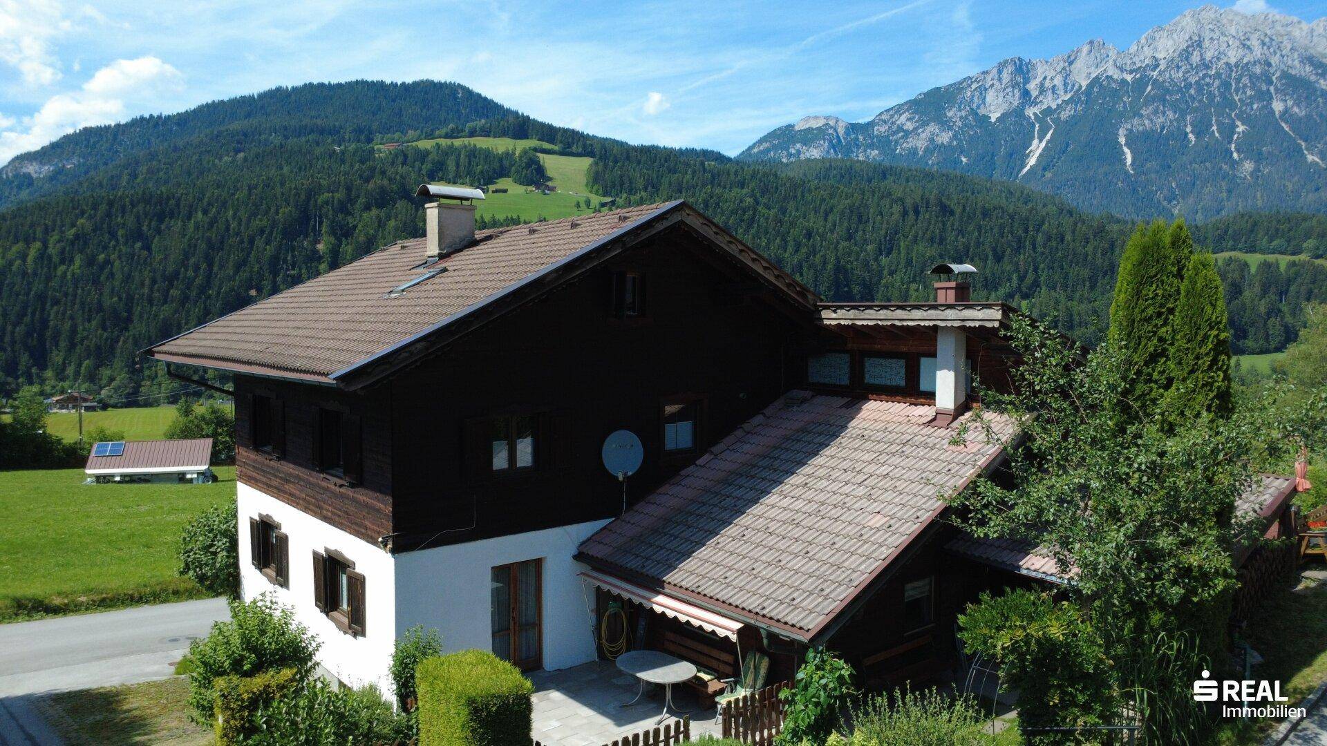 Traditionelles Haus in alpiner Landschaft mit Bergblick und umgeben von grünen Wiesen und Wäldern.