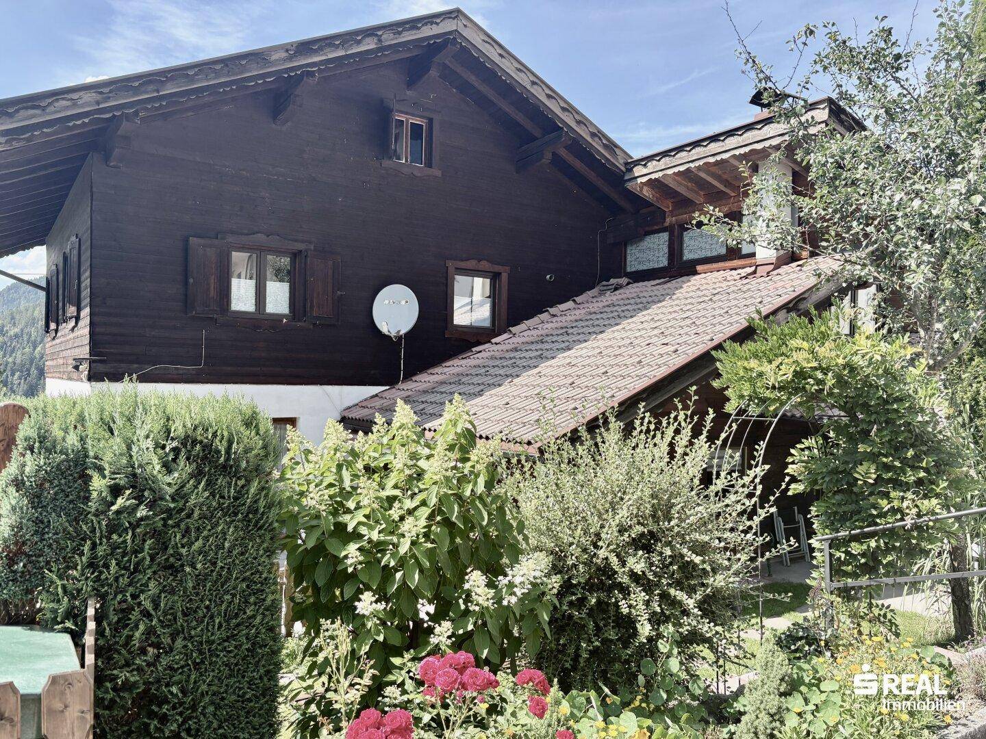 Detailansicht der Hausfassade mit traditioneller Holzverkleidung im oberen Bereich und weißem Putz unten.