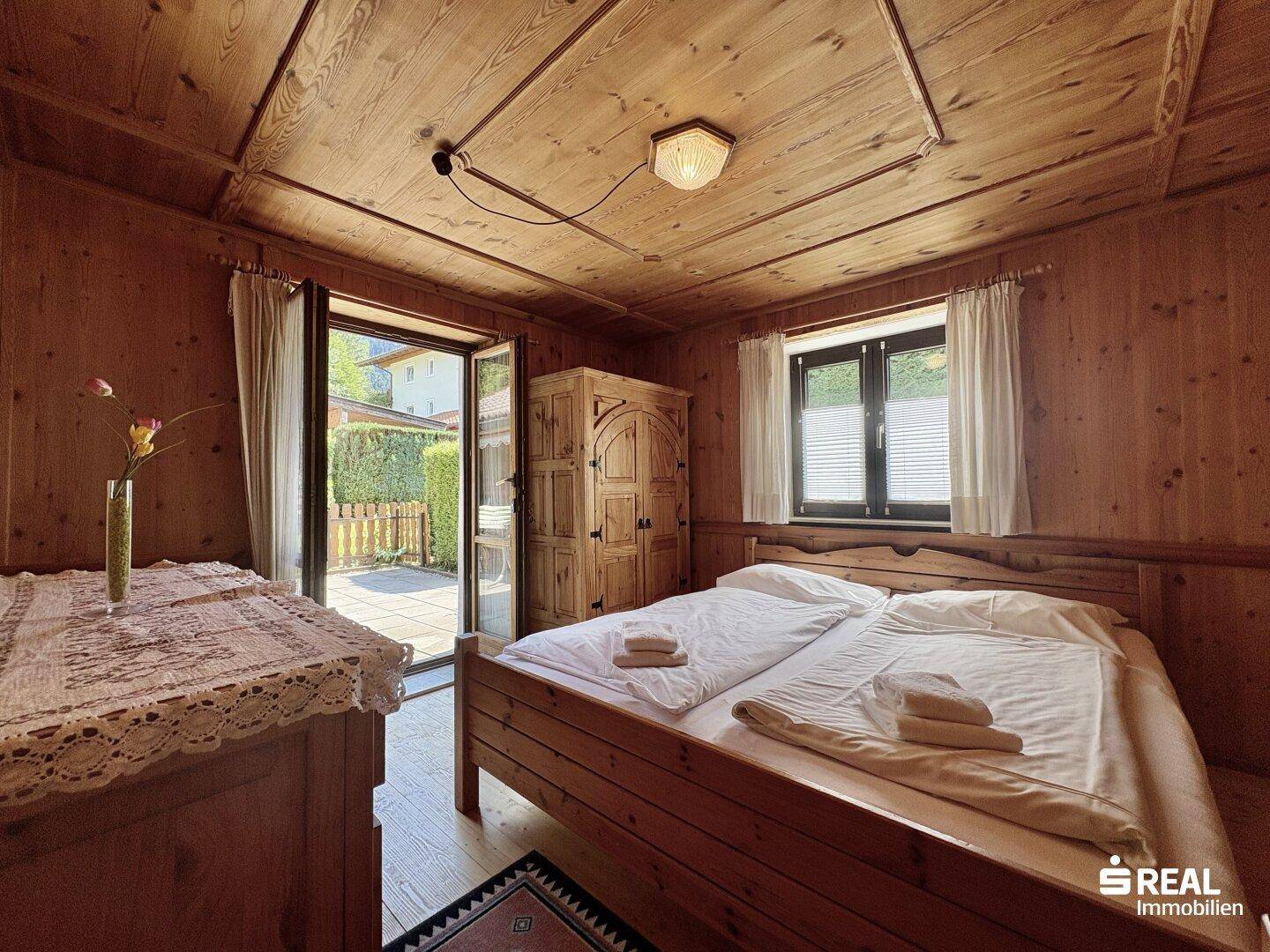 Schlafzimmer im alpinen Stil mit Holztäfelung, Doppelbett und direktem Zugang zu einer kleinen Terrasse.