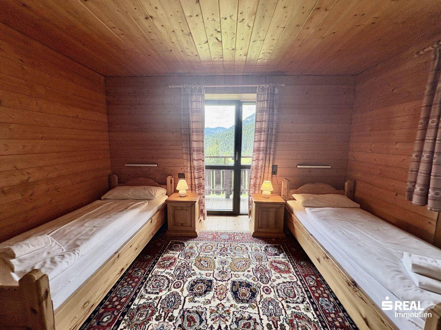 Schlafzimmer mit zwei Einzelbetten, Holztäfelung und Balkonzugang mit herrlichem Bergblick.