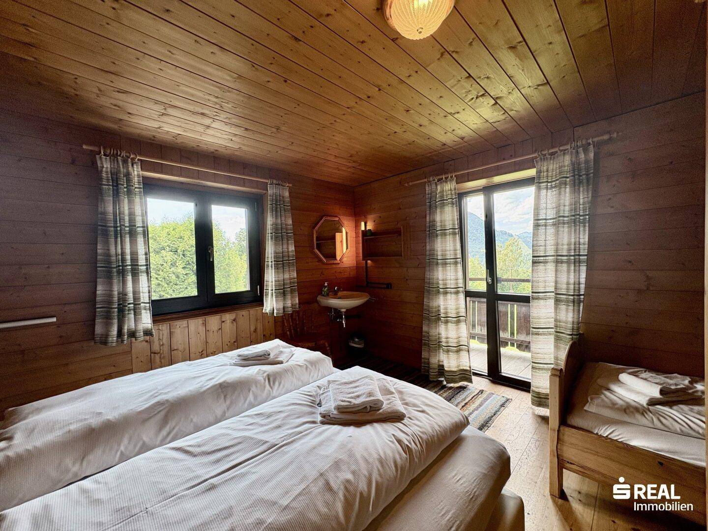 Schlafzimmer mit zwei Einzelbetten, Holztäfelung, eigenem Waschbecken und Balkonzugang mit Bergblick.