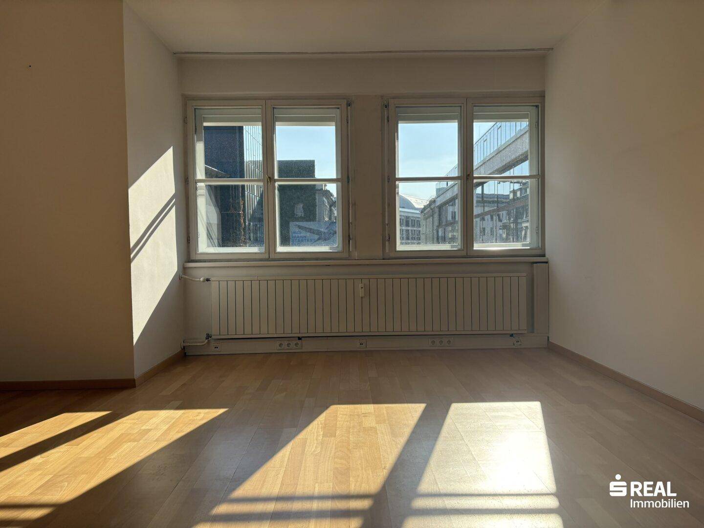 Detailansicht der großen Fenster und des Heizkörpers in einem hellen Büroraum mit Holzboden.