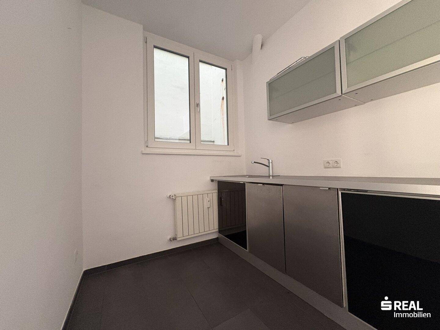 Kleine, moderne Küchenzeile mit dunklen Schränken, Spüle und einem Fenster, ideal für ein Büro.