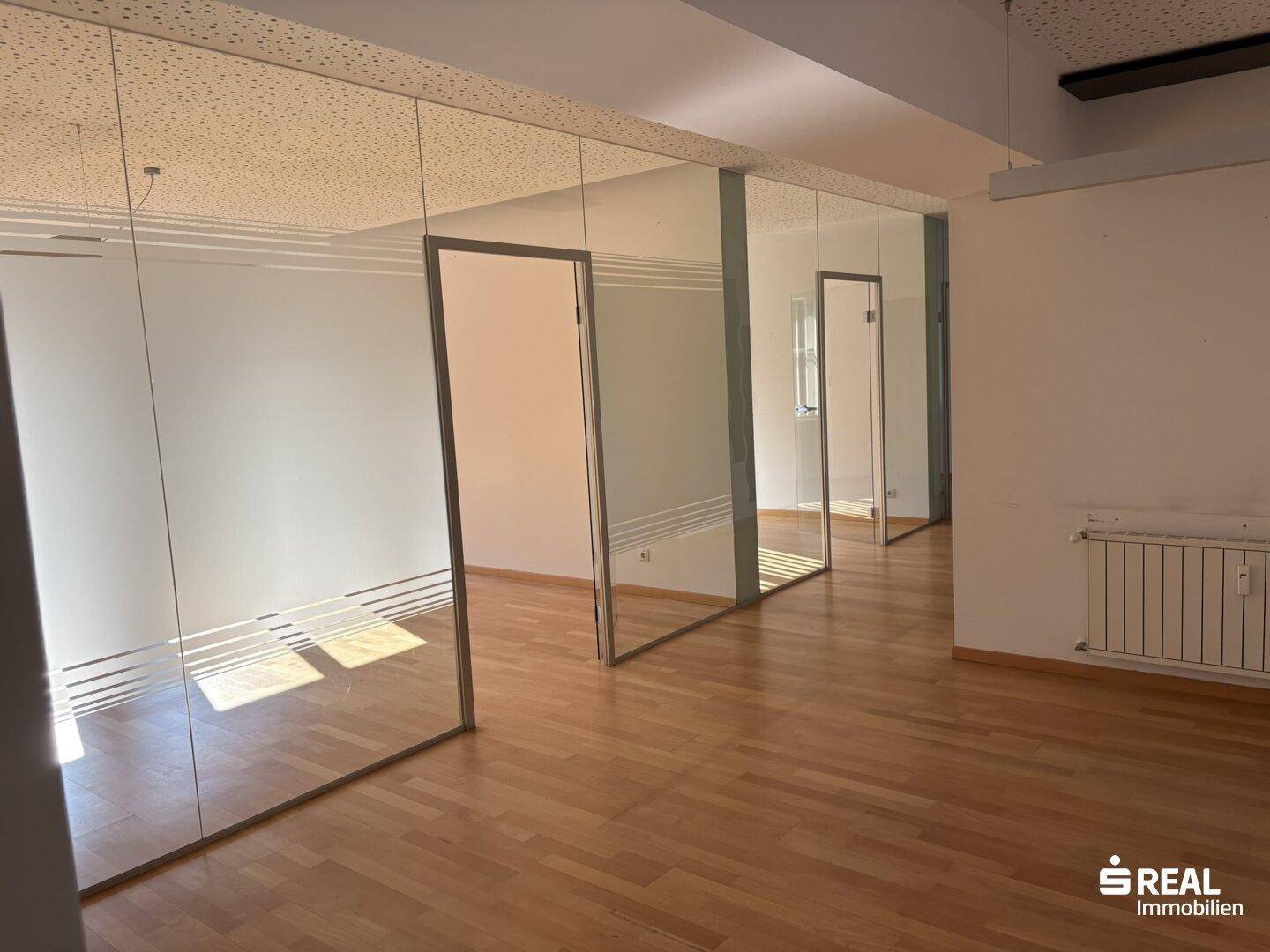 Geräumiges Büro mit Glaswänden, Holzboden und Akustikdecke, ideal für eine moderne Arbeitsumgebung.